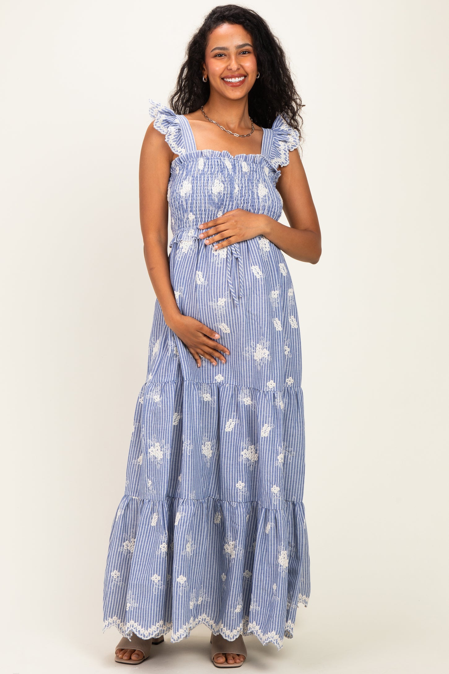 woman wearing a blue and white floral striped maternity maxi dress and holding her baby bump