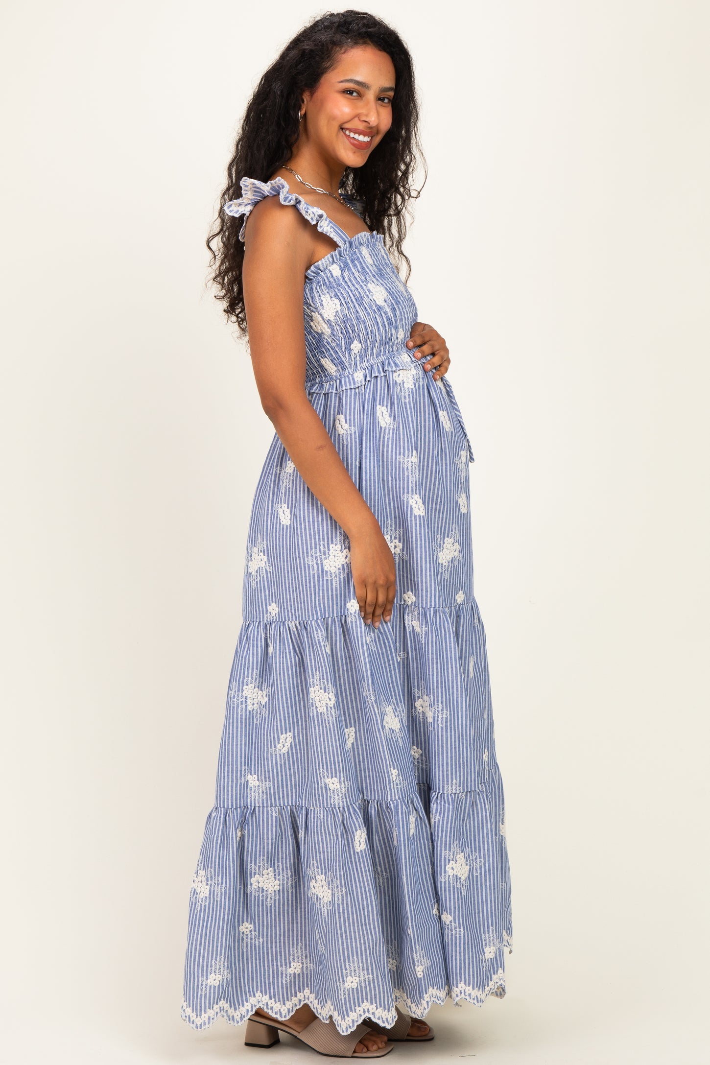 woman wearing a blue and white striped maternity maxi dress with ruffle straps and floral patterns, showing her baby bump