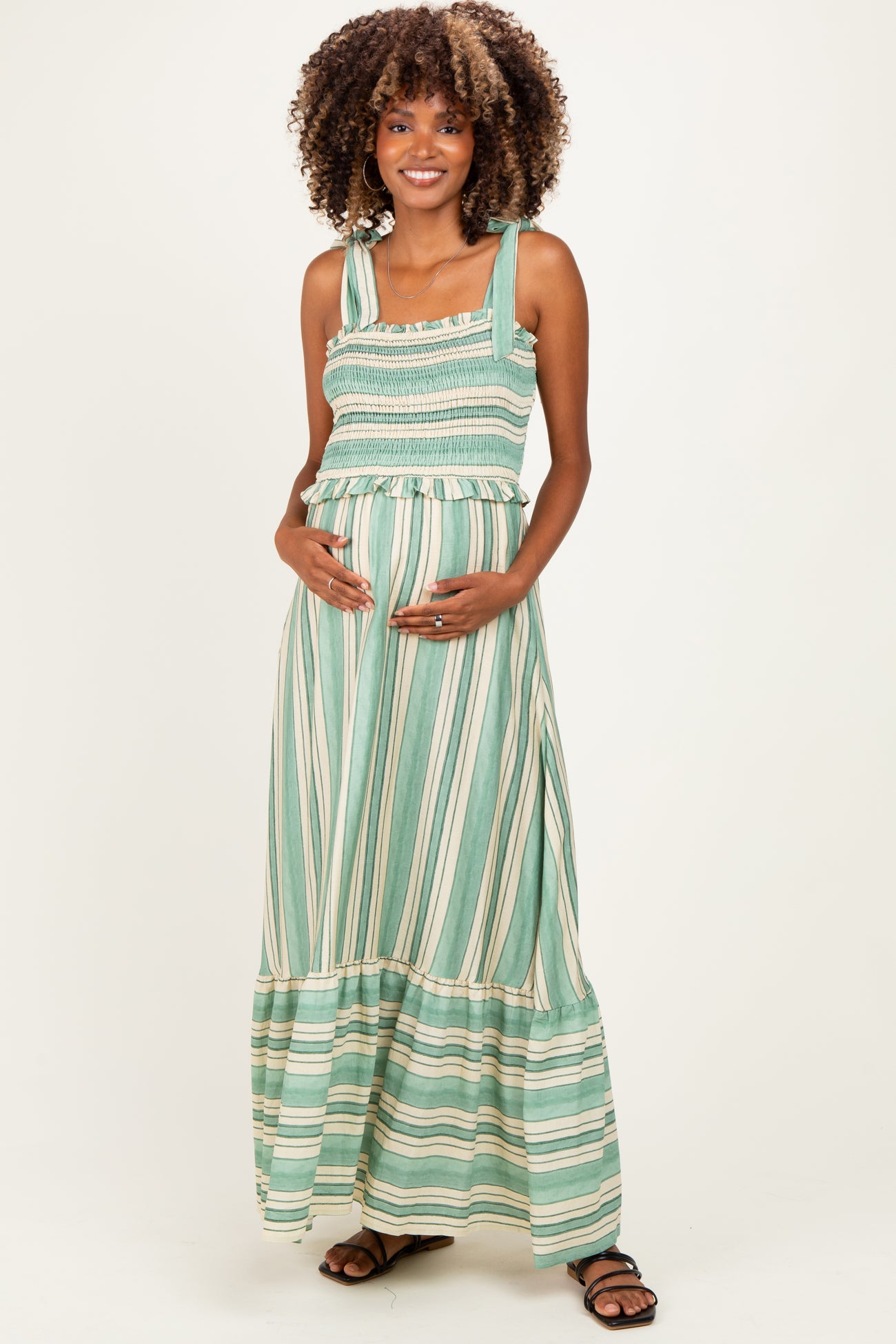 woman wearing a green striped maternity dress with smocked bodice and flowy skirt, holding her baby bump