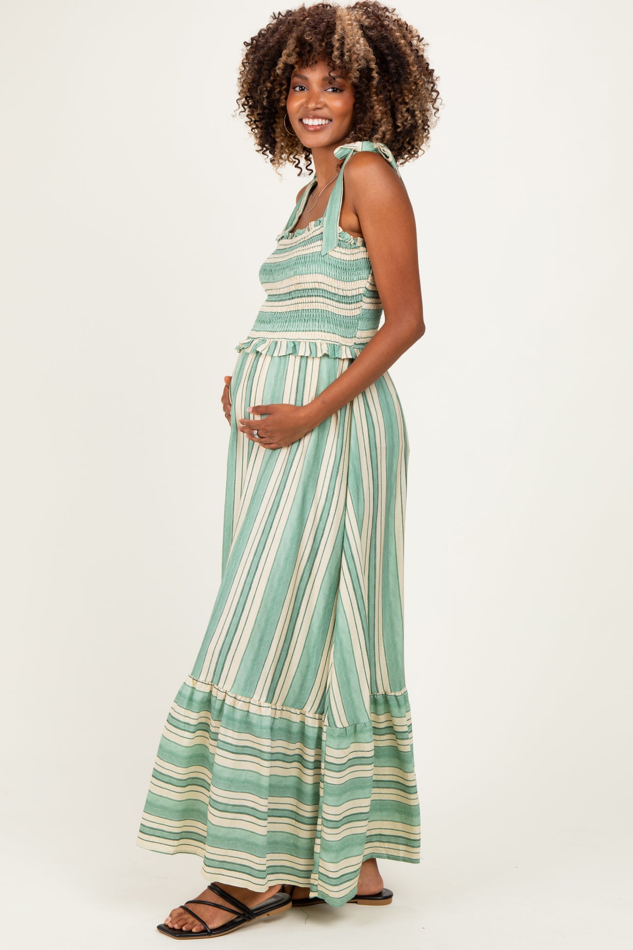 woman wearing a green and white striped maternity maxi dress with smocked bodice and ruffled hem, showing her baby bump