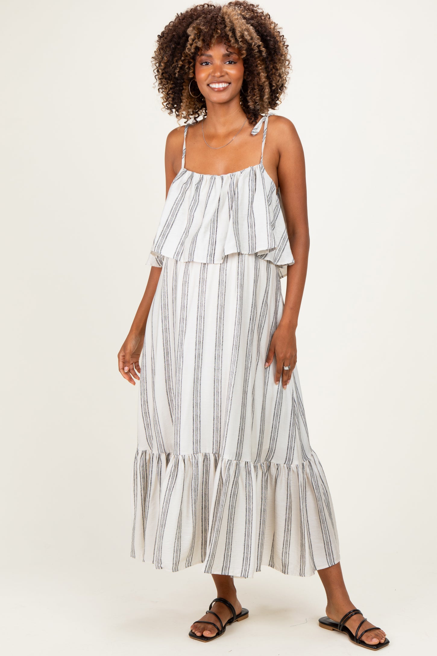 woman wearing a striped white maternity maxi dress with ruffled layers and spaghetti straps