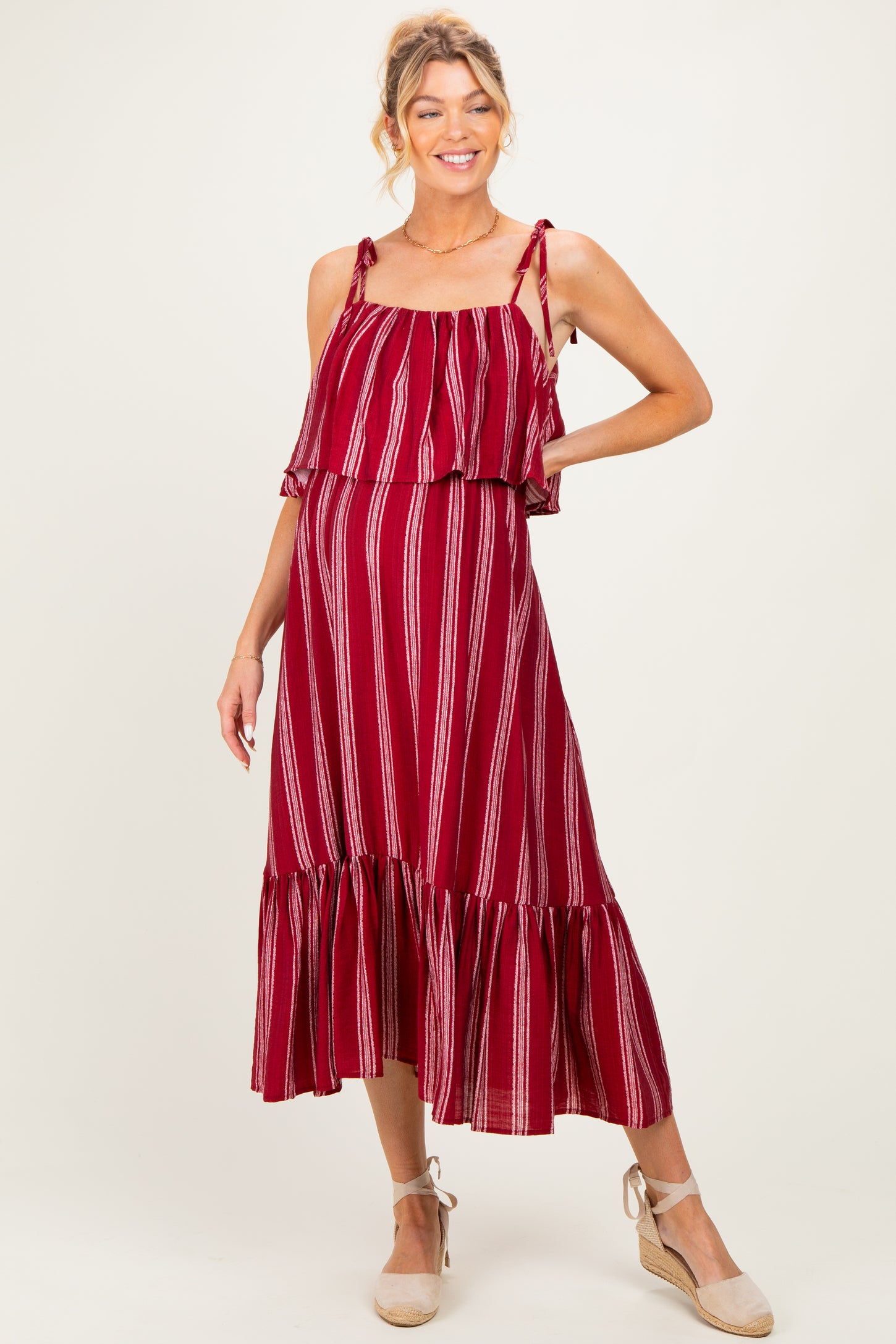 woman wearing a burgundy striped maternity maxi dress with ruffle straps and a tiered hem, showcasing her baby bump
