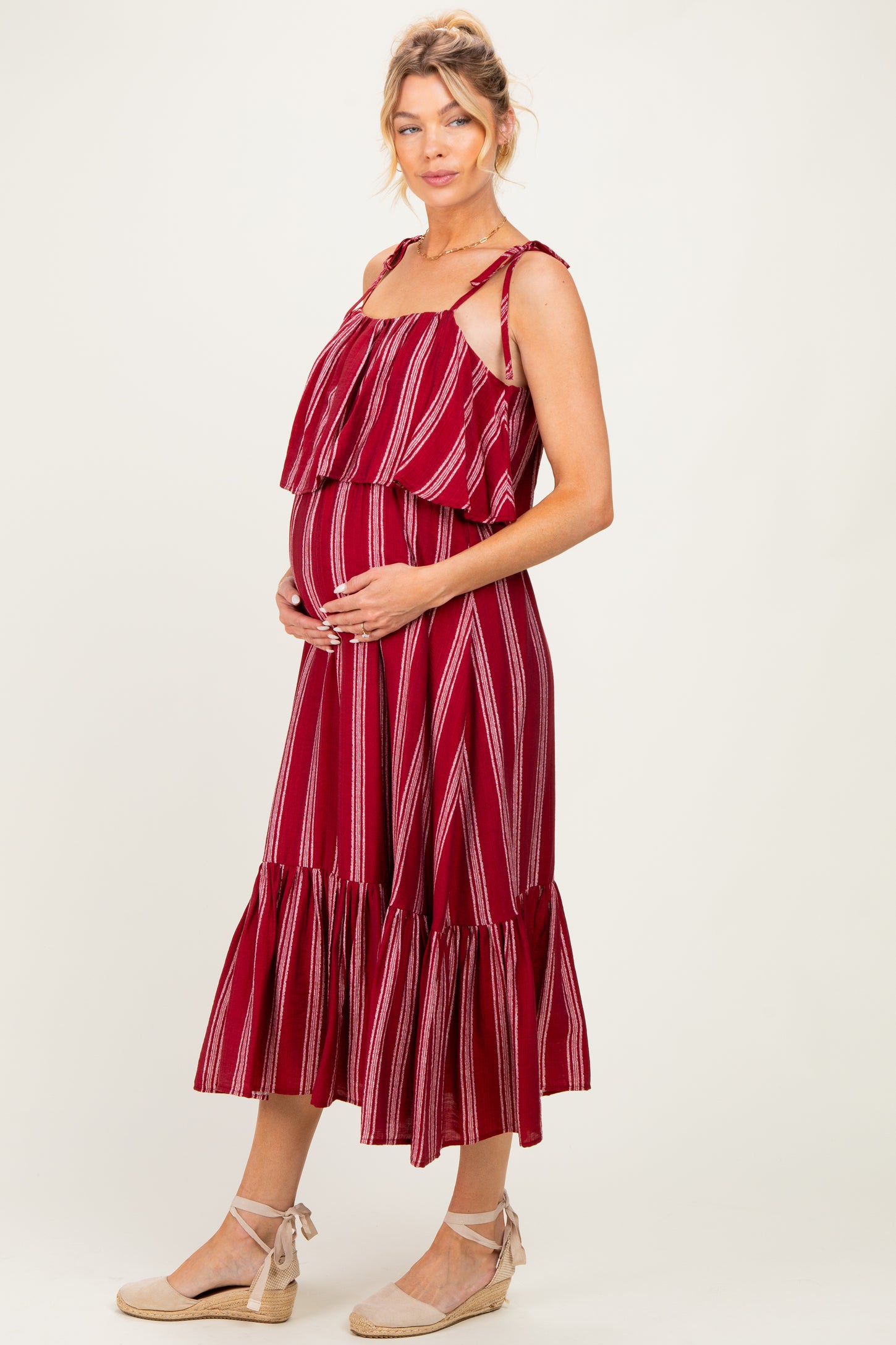 woman wearing a red striped maternity dress with ruffled layers and a flowy hem, cradling her baby bump