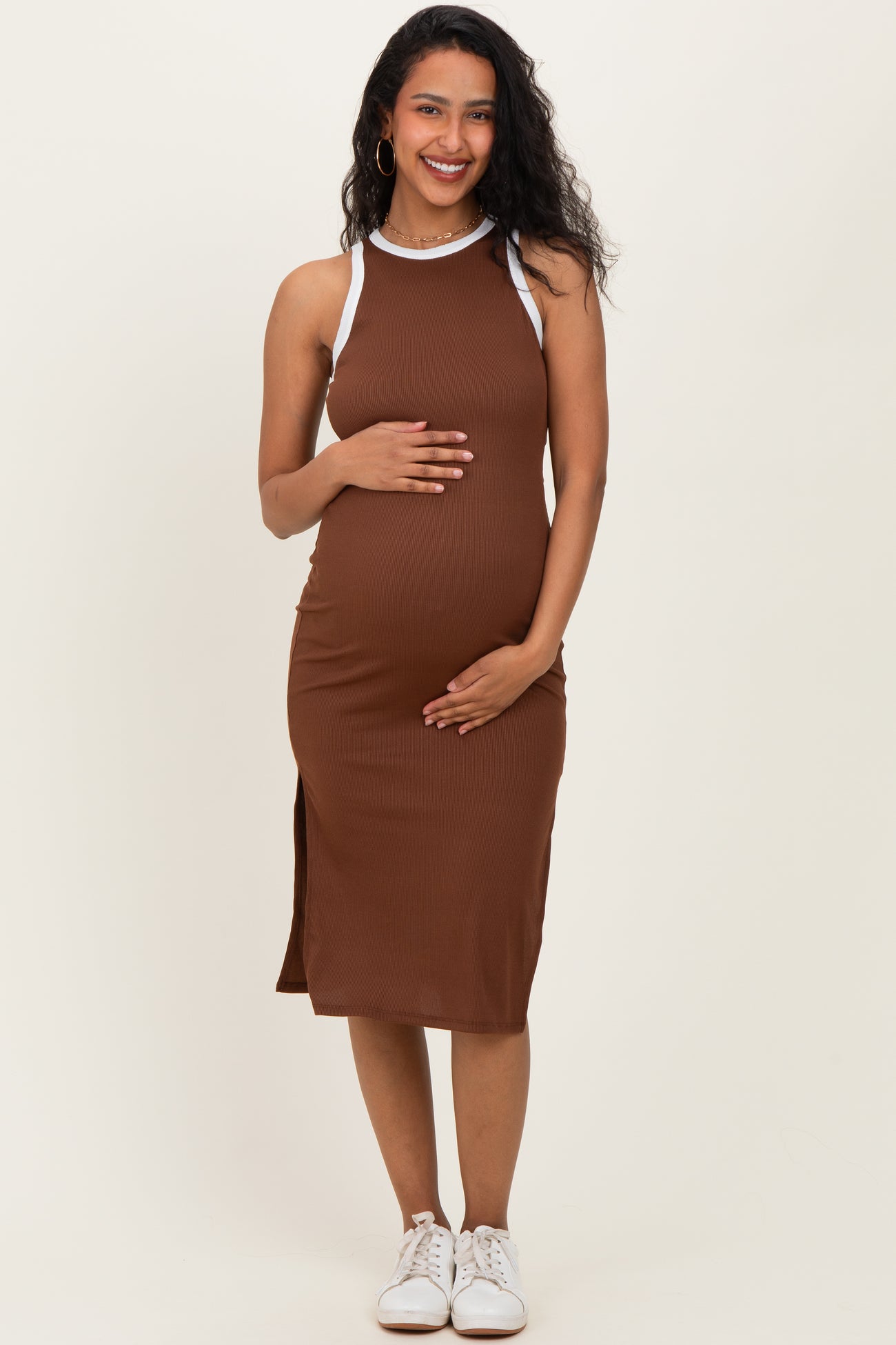 woman wearing a brown maternity dress with white straps, showcasing her baby bump and smiling