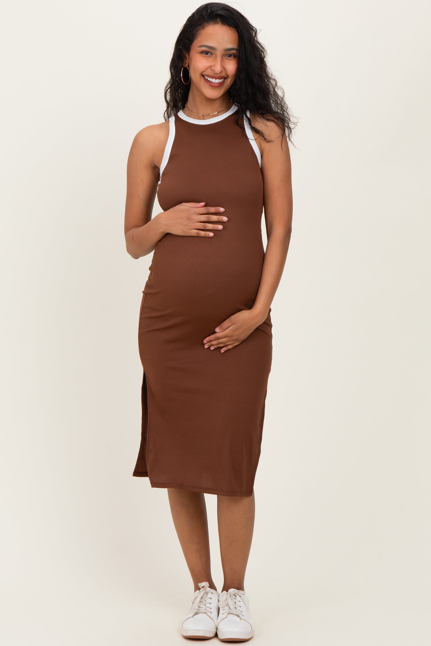 woman wearing a brown maternity dress with white straps, showcasing her baby bump and smiling