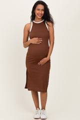 woman wearing a brown maternity dress with white straps, showcasing her baby bump and smiling