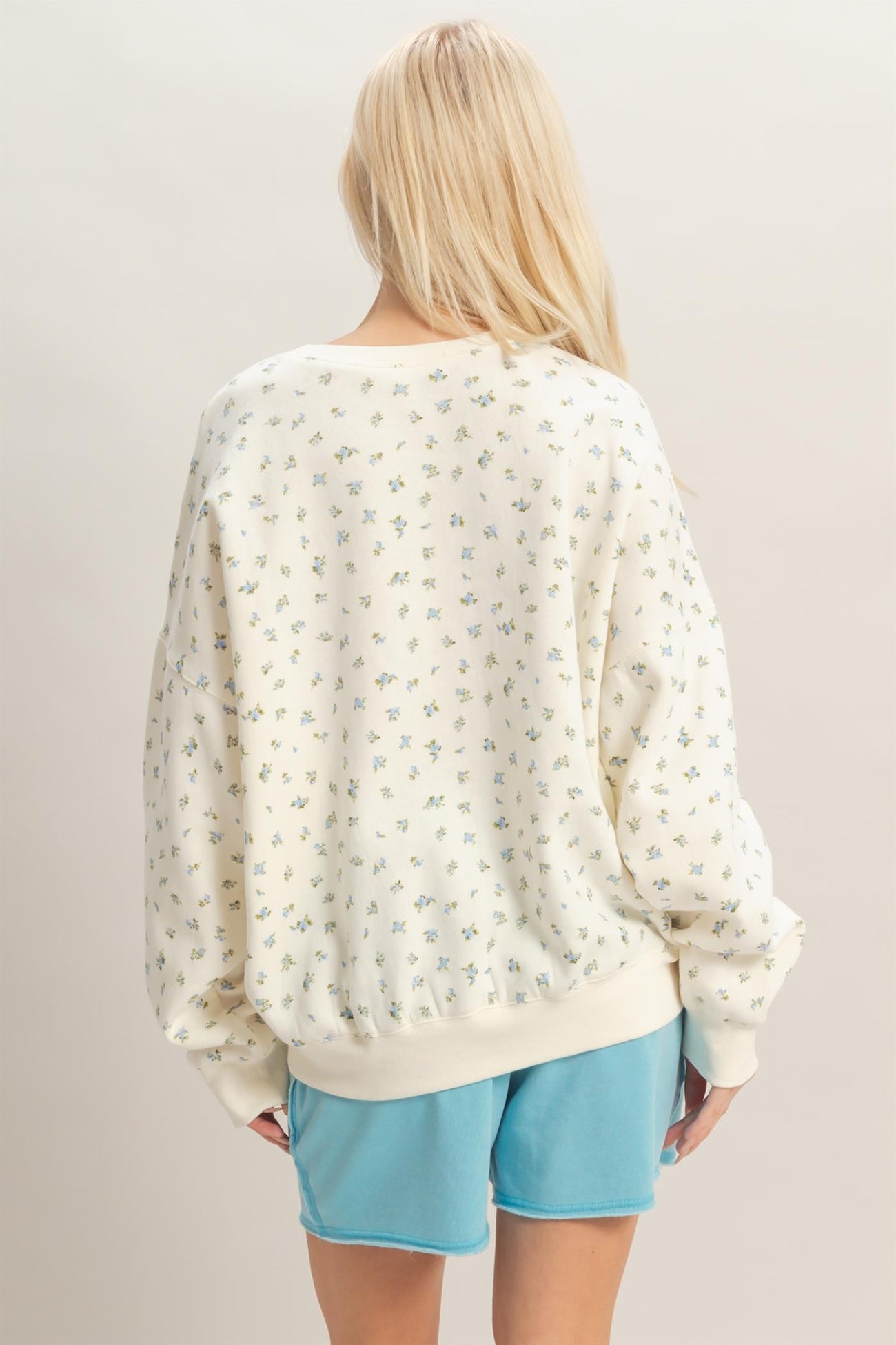 woman wearing a cream oversized sweatshirt with small floral print and light blue shorts, viewed from the back
