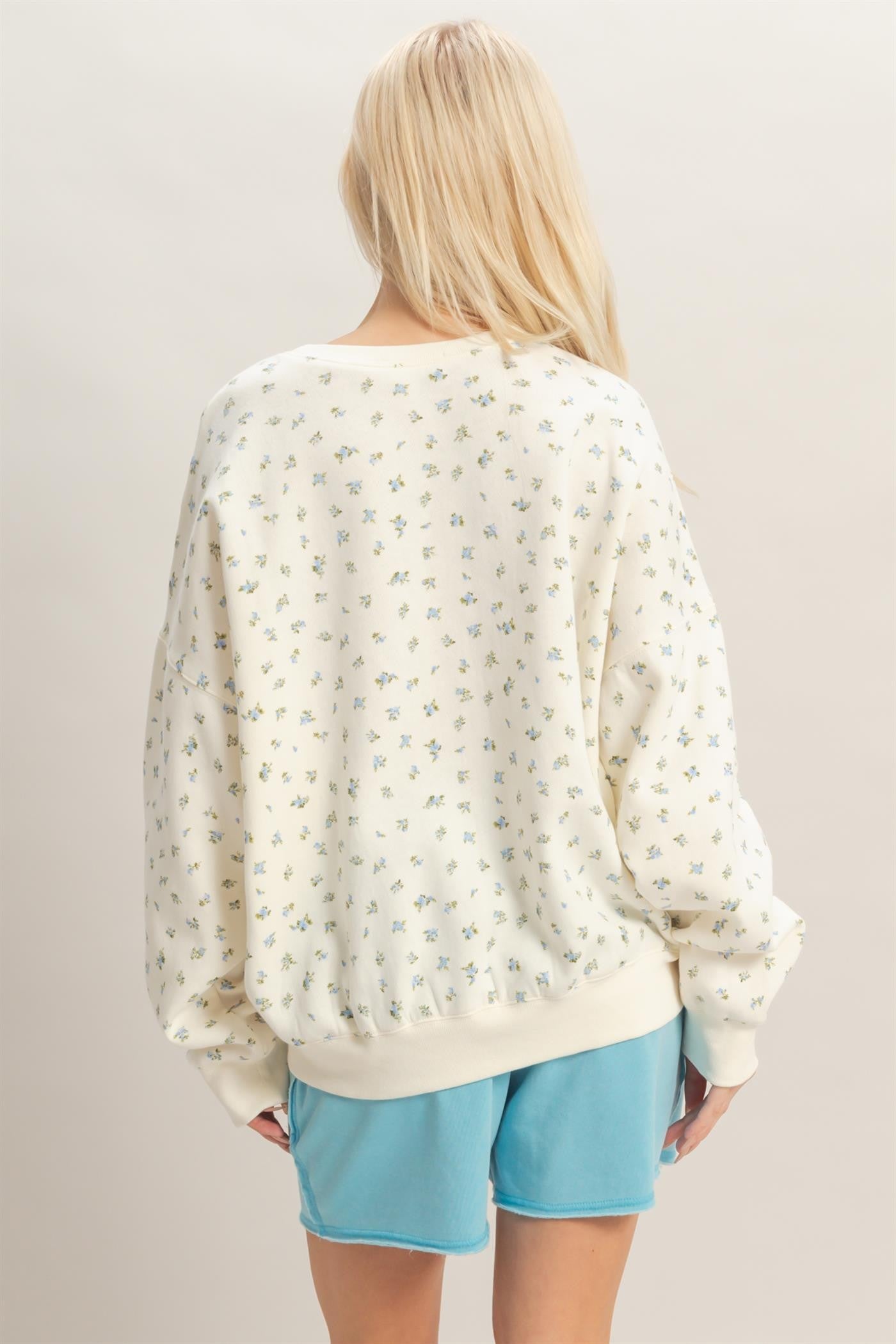 woman wearing a cream oversized sweatshirt with small floral print and light blue shorts, viewed from the back