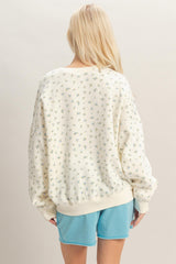 woman wearing a cream oversized sweatshirt with small floral print and light blue shorts, viewed from the back