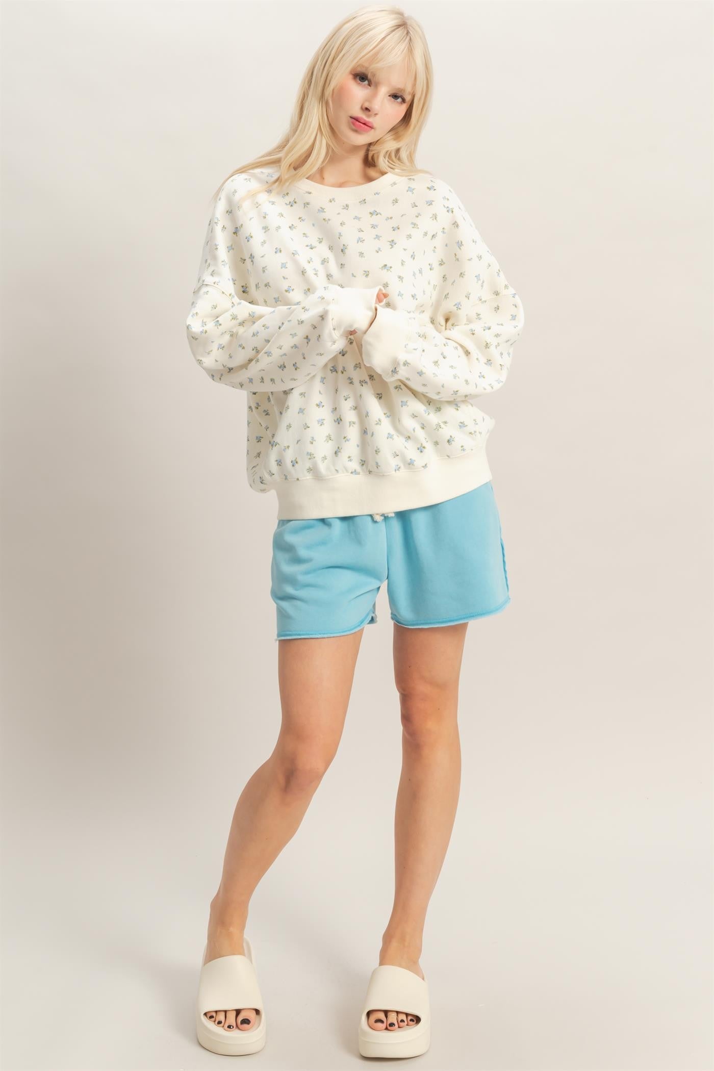 woman wearing a cream floral print oversized sweatshirt and light blue shorts, styled with cream slide-on sandals
