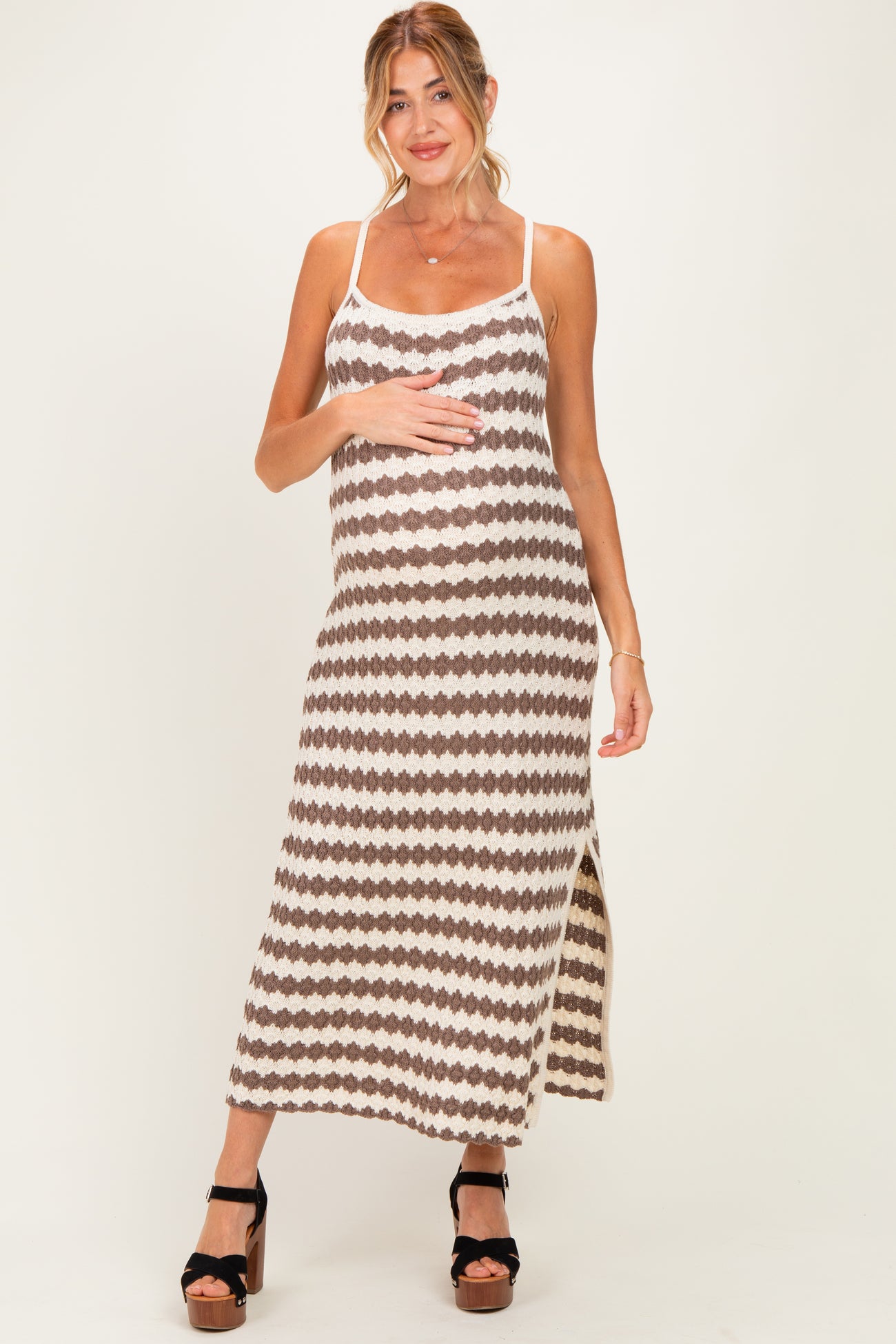 woman wearing a brown and cream patterned maternity maxi dress with a side slit and holding her baby bump