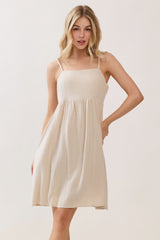 woman wearing a beige sleeveless sundress with a fitted bodice and flared skirt.