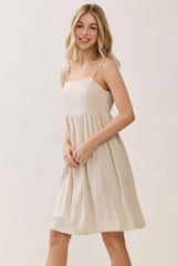 woman wearing a lightweight beige spaghetti strap dress with a flowing skirt and fitted bodice