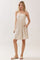 woman wearing a beige sleeveless sundress with a gathered waist and pockets, standing against a light background