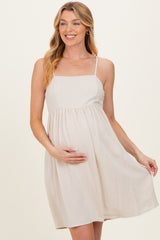 woman wearing a beige maternity dress with spaghetti straps and a flowing design, holding her baby bump