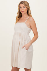 woman wearing a beige maternity dress with adjustable spaghetti straps and pockets, highlighting her baby bump