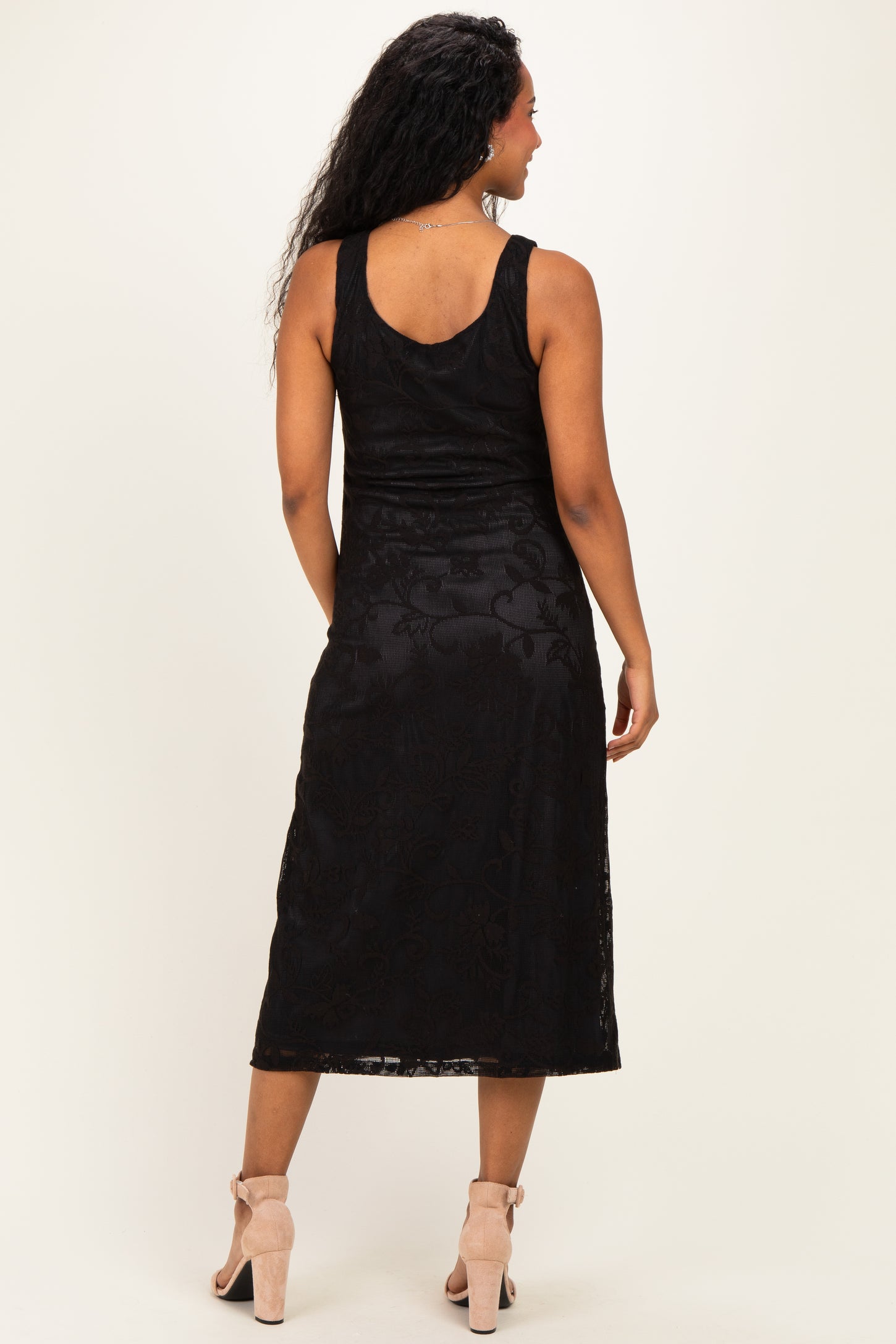 woman wearing a black lace midi maternity dress, showing the back view and styled with light pink heels