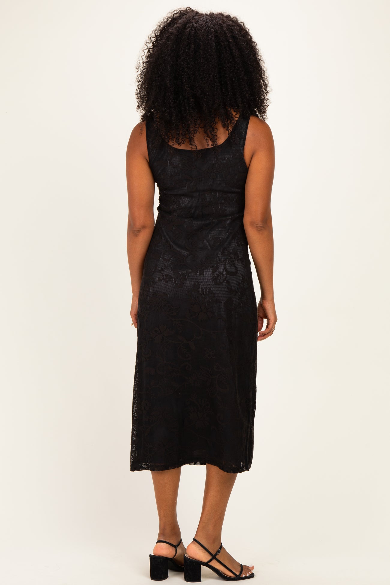 woman wearing a black sleeveless midi dress with a floral pattern and a fitted silhouette, viewed from the back