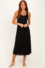 woman wearing a black sleeveless midi dress with a floral lace overlay and standing on a light background