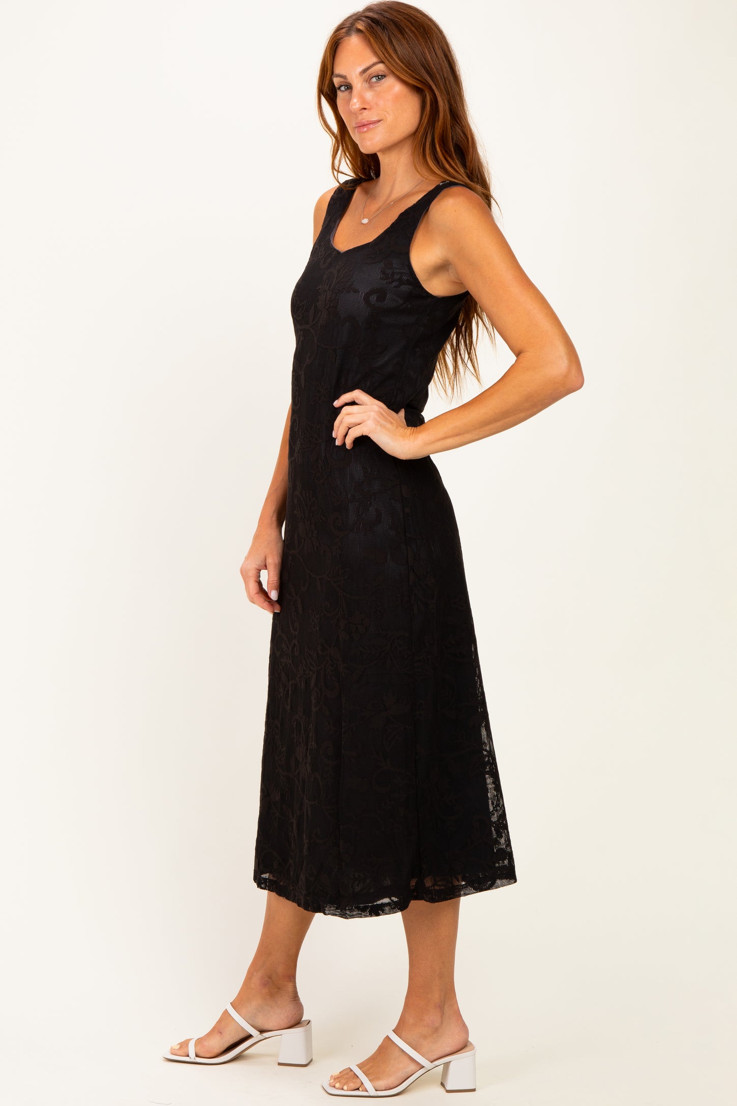 woman wearing a black sleeveless midi dress with a lace overlay and standing in a side profile position