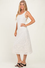woman wearing a white midi dress with floral embroidery and adjustable straps, standing sideways with a smile