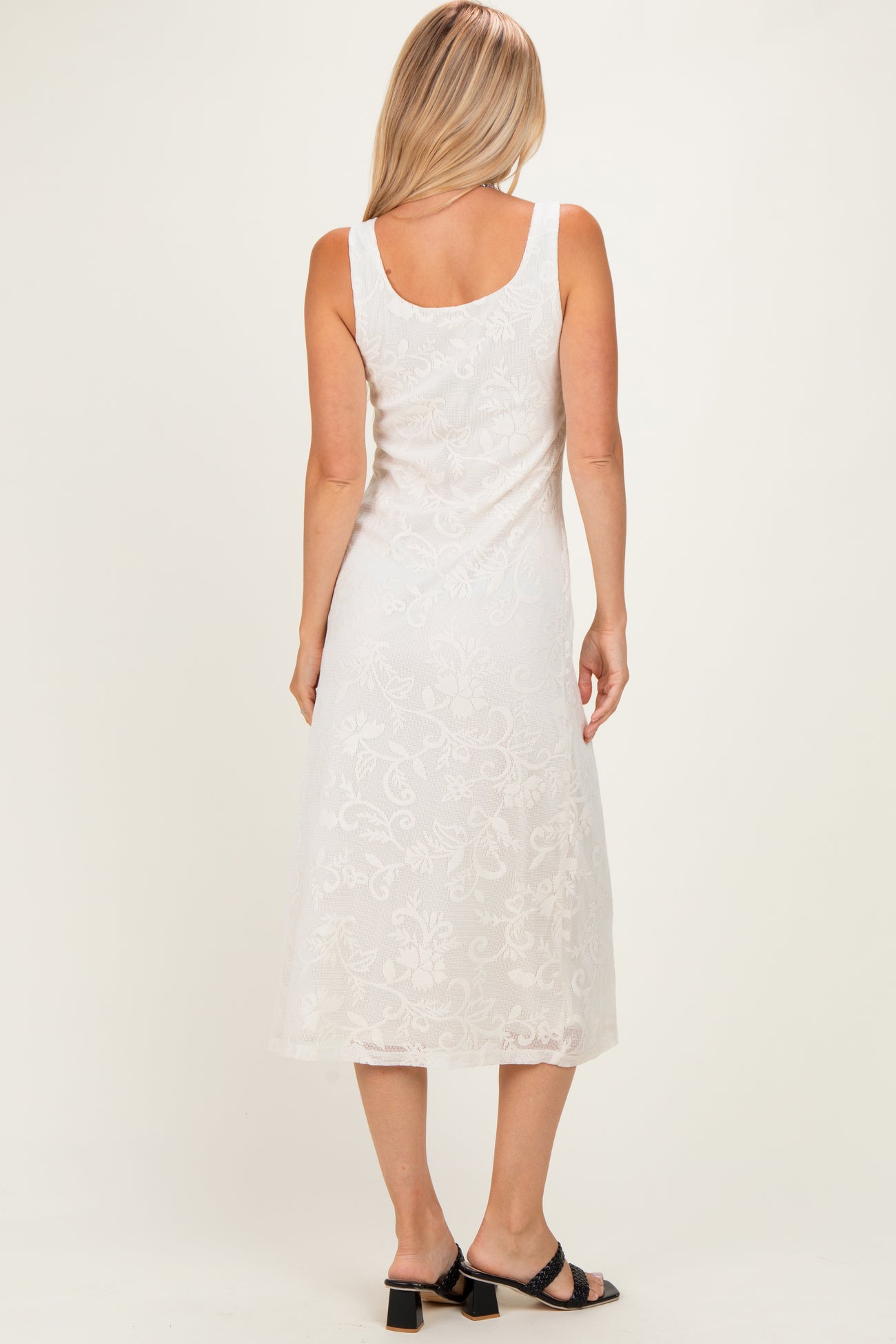 woman wearing a white sleeveless lace midi dress, showing a floral design and back view
