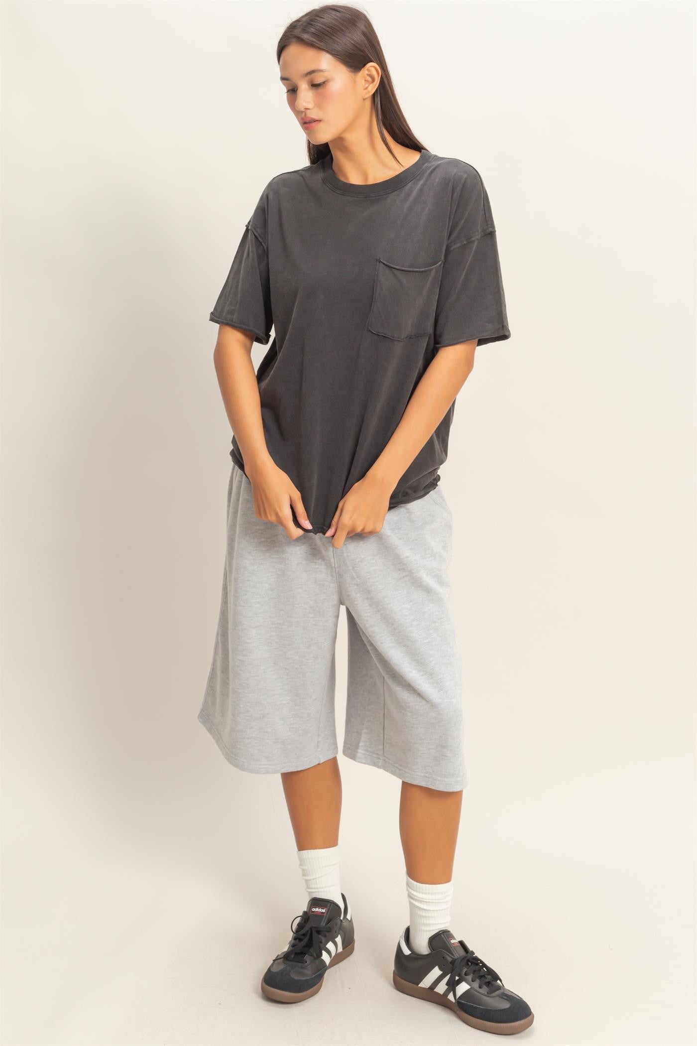 woman wearing a loose black t-shirt with a pocket and gray knee-length shorts, styled with sneakers and socks