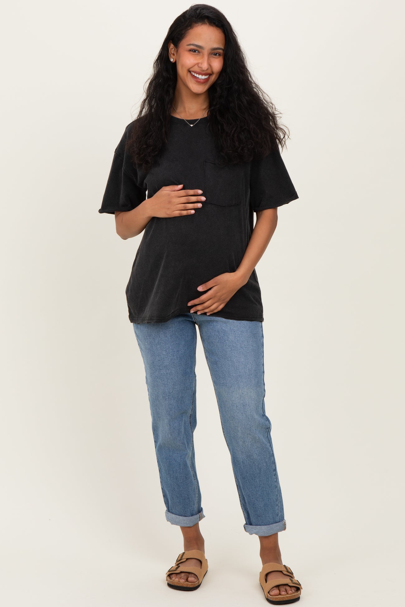 woman wearing a black short sleeve maternity top and blue rolled cuff maternity jeans, holding her baby bump