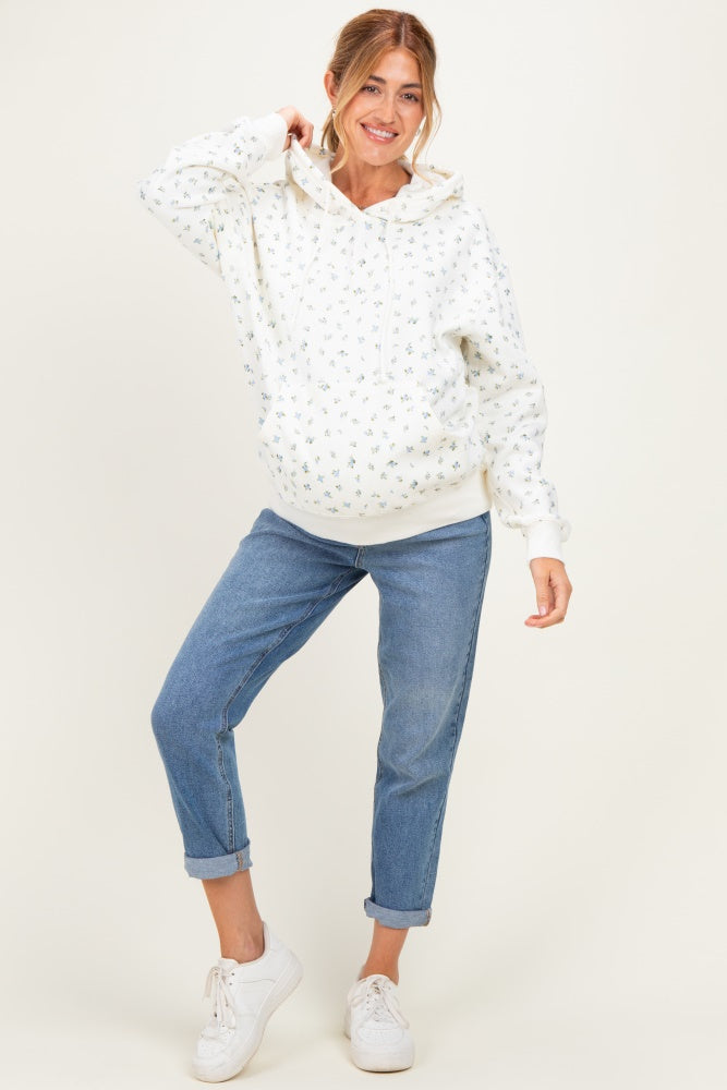 woman wearing a white floral printed maternity hoodie and blue rolled-up jeans, showcasing her baby bump