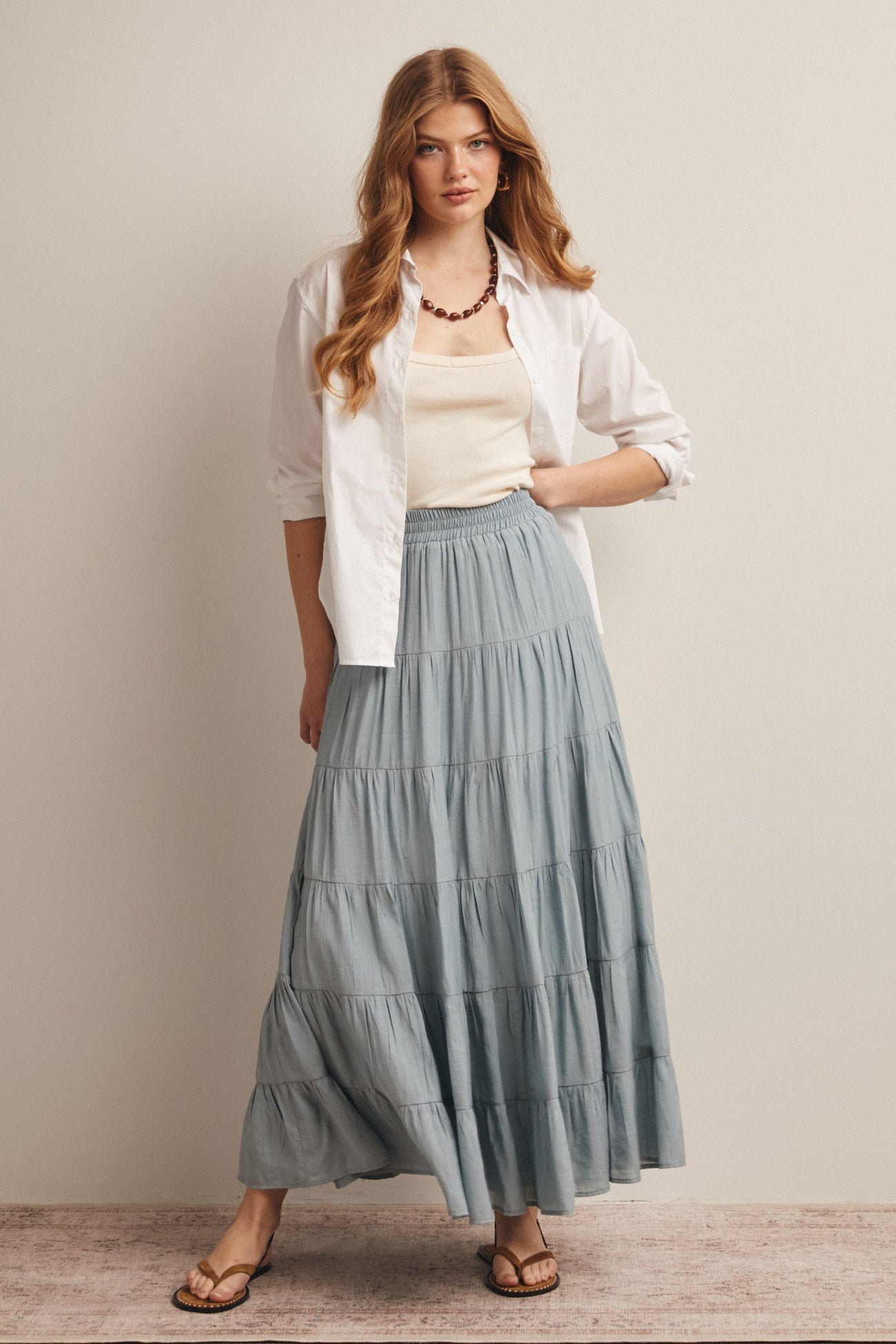 woman wearing a white button-up shirt and a light blue tiered maxi skirt with flat sandals and a statement necklace