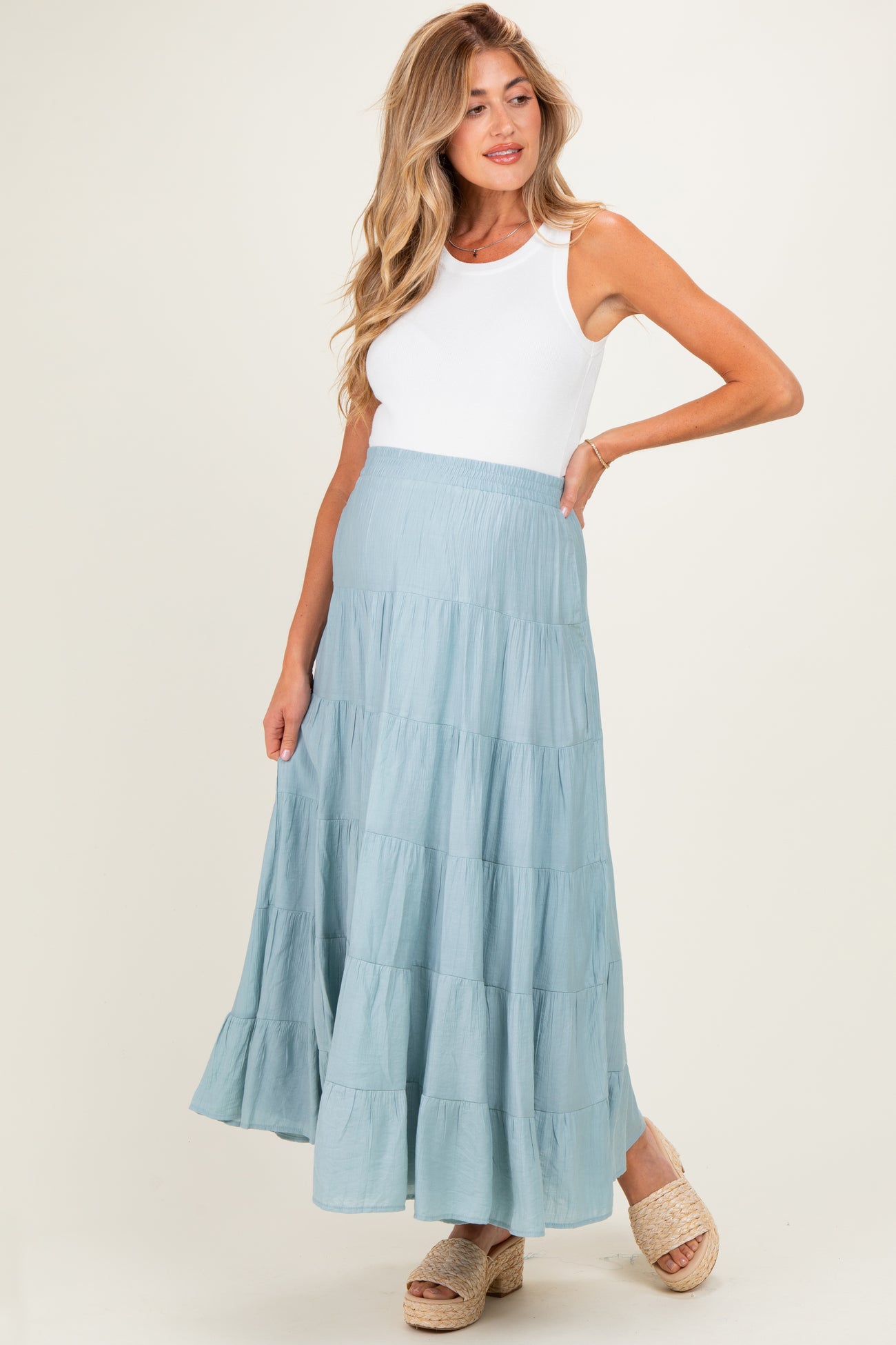woman wearing a light blue tiered maternity maxi skirt and a white tank top, showing her baby bump