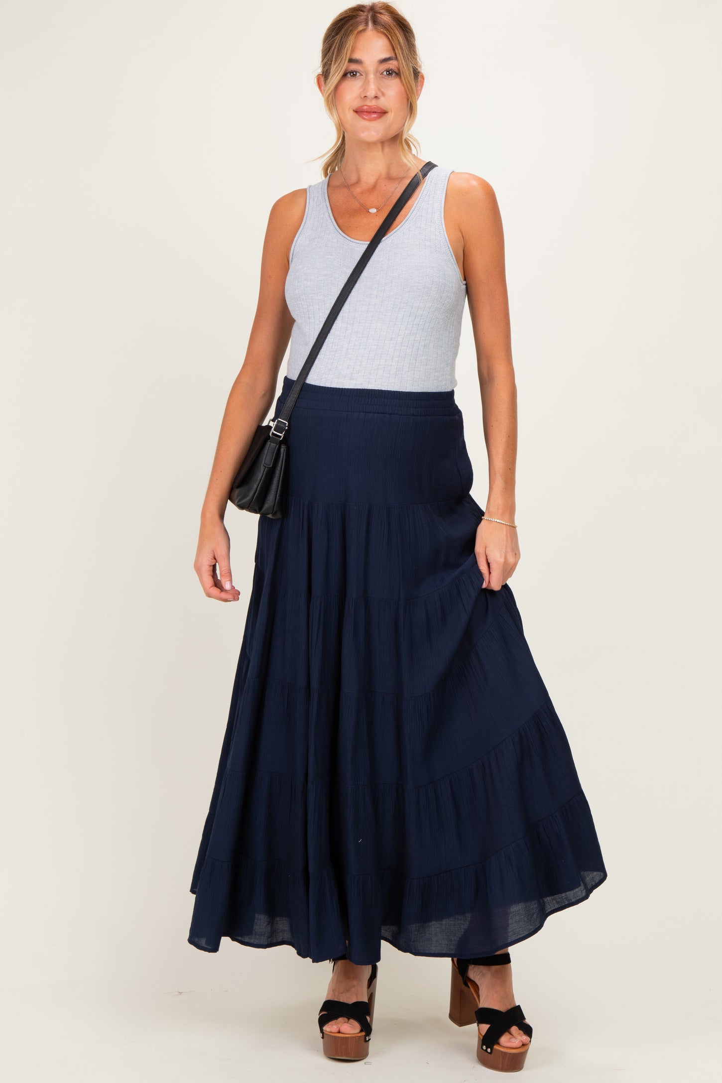 woman wearing a gray tank top and a navy blue tiered maternity maxi skirt with a black handbag