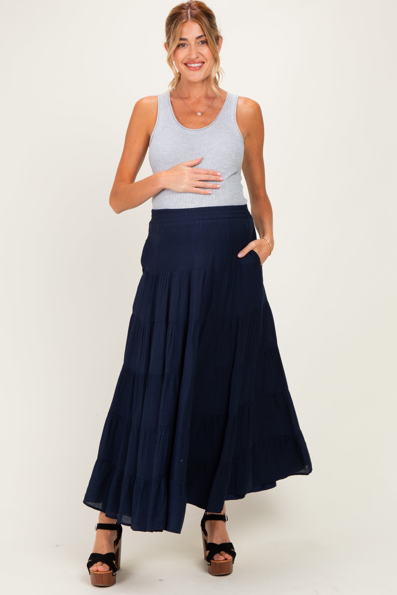 woman wearing a gray tank top and a navy tiered maxi skirt, holding her baby bump