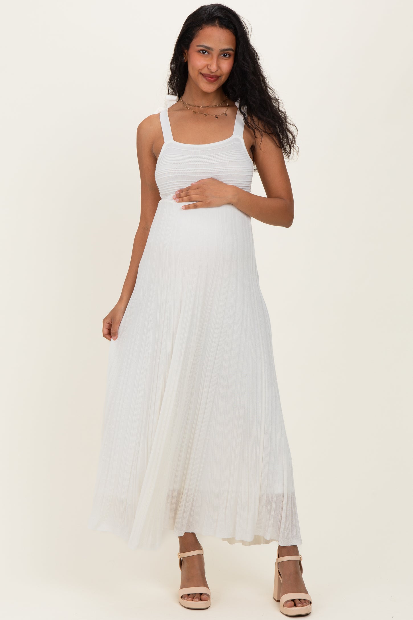 woman wearing a white pleated maternity dress and gently holding her baby bump