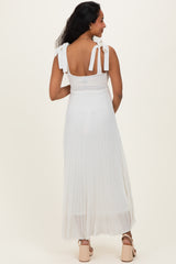 woman wearing a white pleated maternity dress with tie shoulder straps, showing her back and flowing skirt