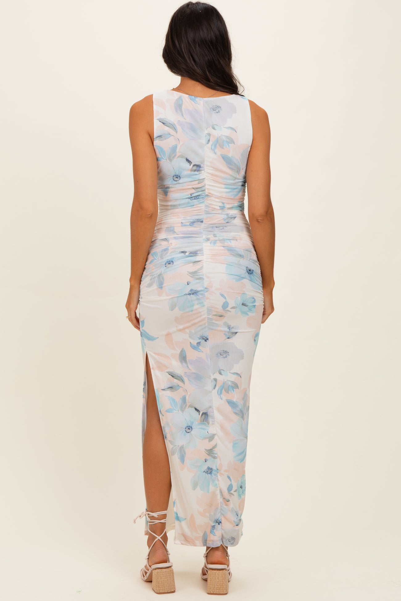 woman wearing a sleeveless floral print maxi dress with side slits and ruched detailing, viewed from the back