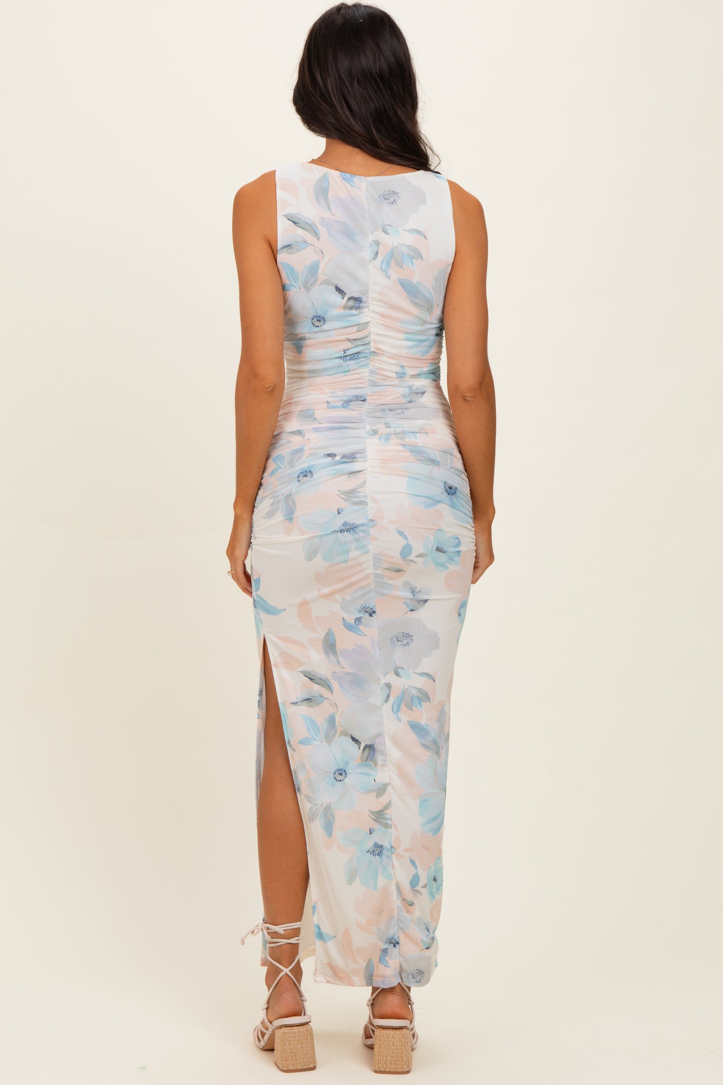 woman wearing a sleeveless floral print maxi dress with side slits and ruched detailing, viewed from the back