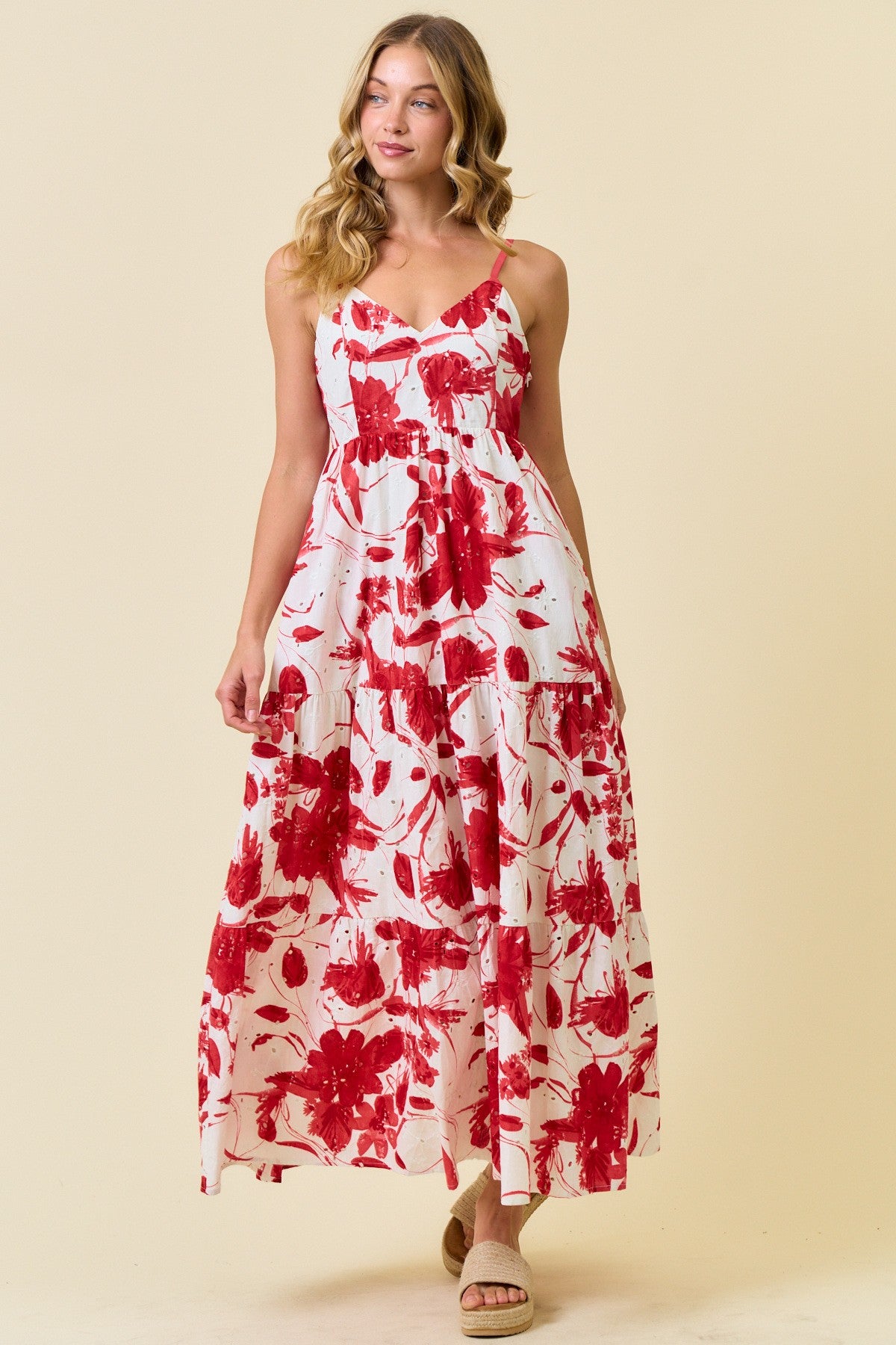 woman wearing a white maxi dress with red floral print and spaghetti straps, standing against a light background