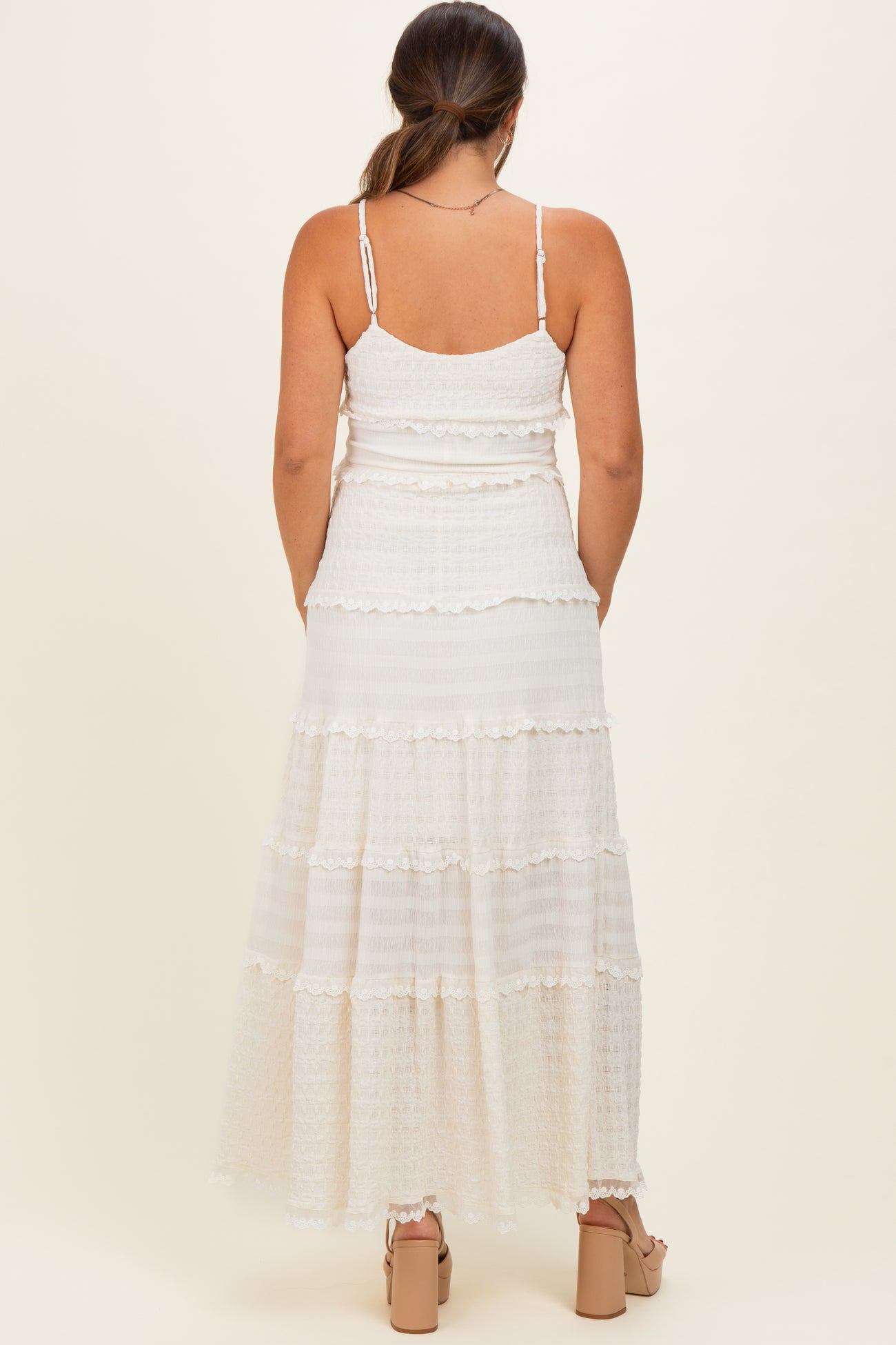 woman wearing a white maternity maxi dress with tiered ruffles and adjustable spaghetti straps, showing a baby bump
