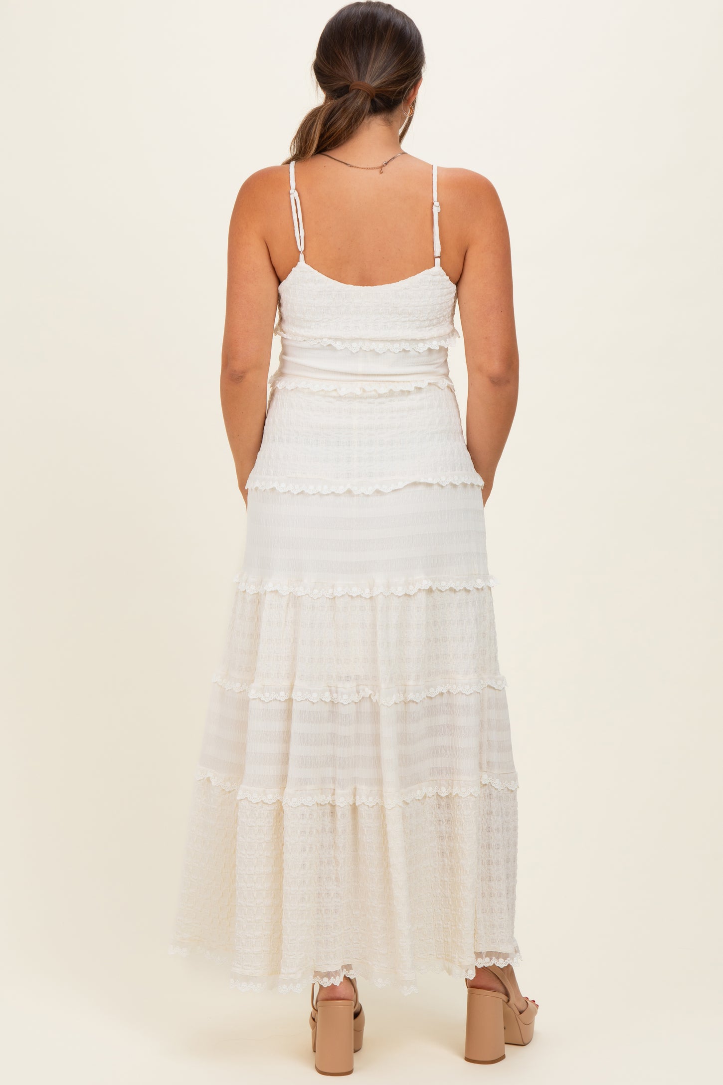 woman wearing a white maternity maxi dress with tiered ruffles and adjustable spaghetti straps, showing a baby bump