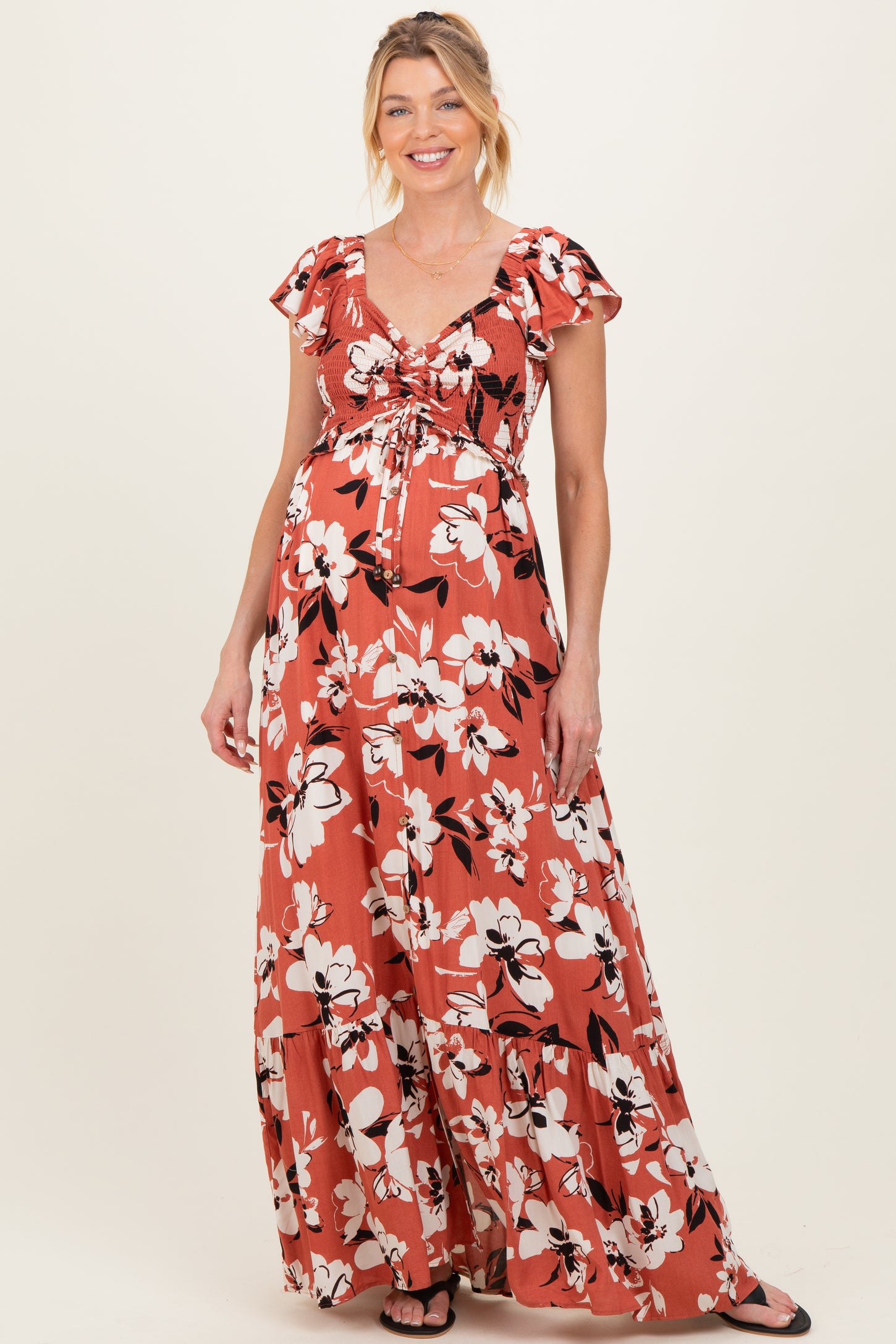 woman wearing a rust floral maxi maternity dress with a ruched bodice and short ruffled sleeves, showcasing her baby bump