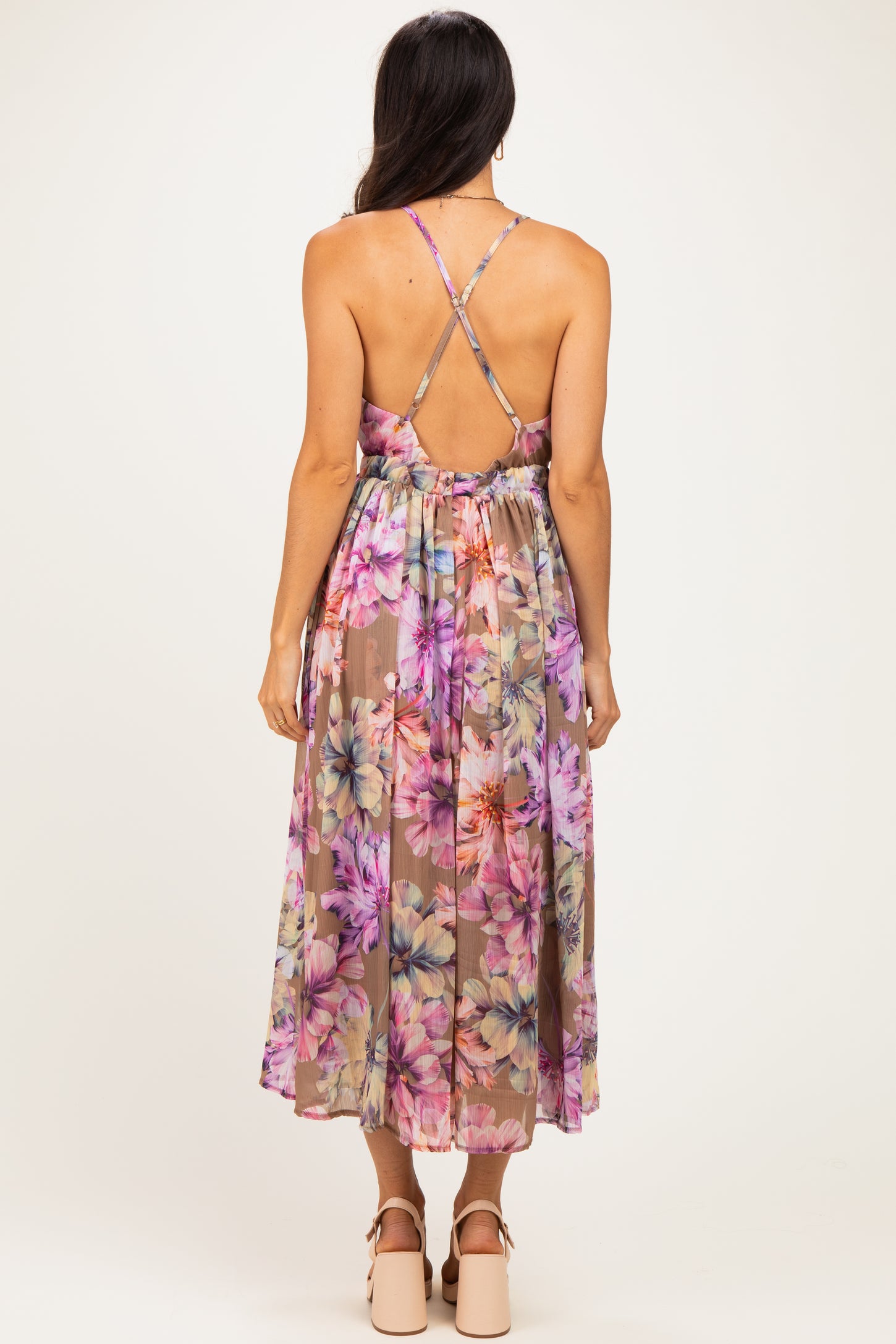 woman wearing a backless floral maxi dress with a crisscross strap design in shades of pink and purple