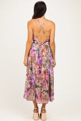 woman wearing a backless floral maxi dress with a crisscross strap design in shades of pink and purple