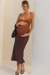 woman wearing a brown and mustard ombre maternity dress, cradling her baby bump against a backdrop