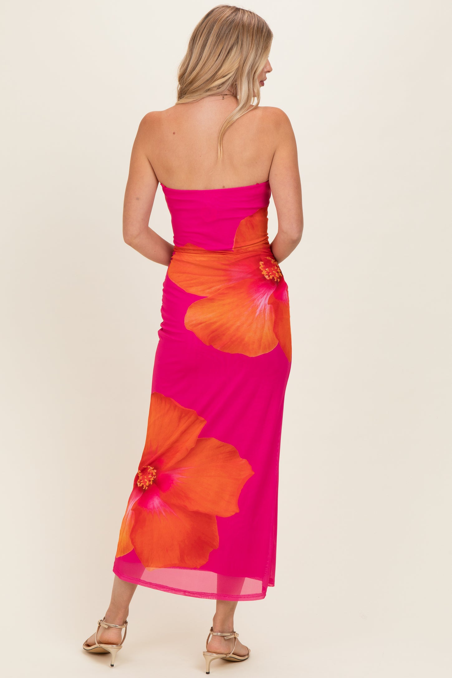 woman wearing a vibrant pink strapless dress with large orange floral design and ruched detailing on the side