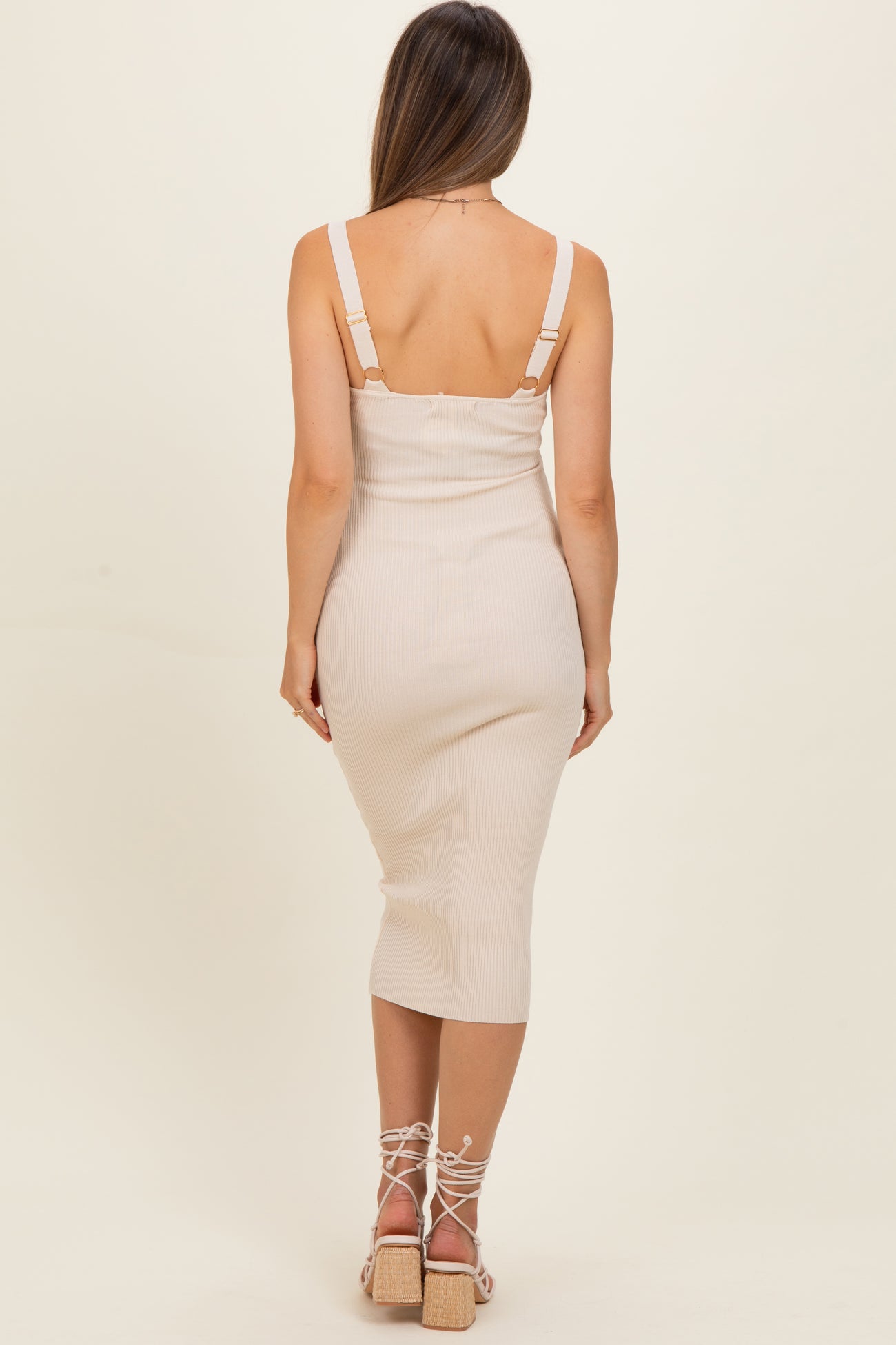 woman wearing a beige ribbed midi maternity dress with adjustable straps, showing a fitted silhouette and back view