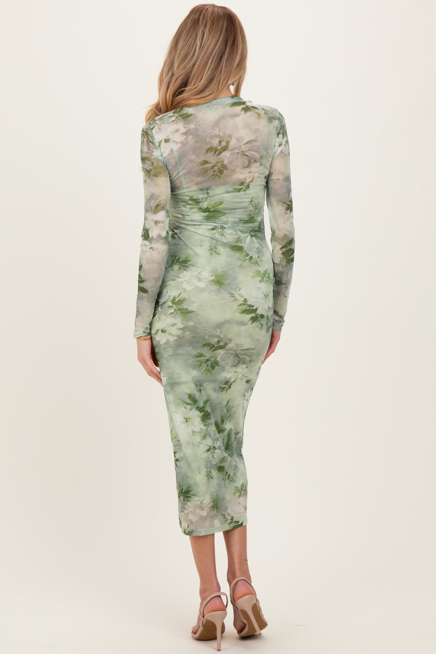 woman wearing a green floral print maternity dress with long sleeves and a fitted silhouette