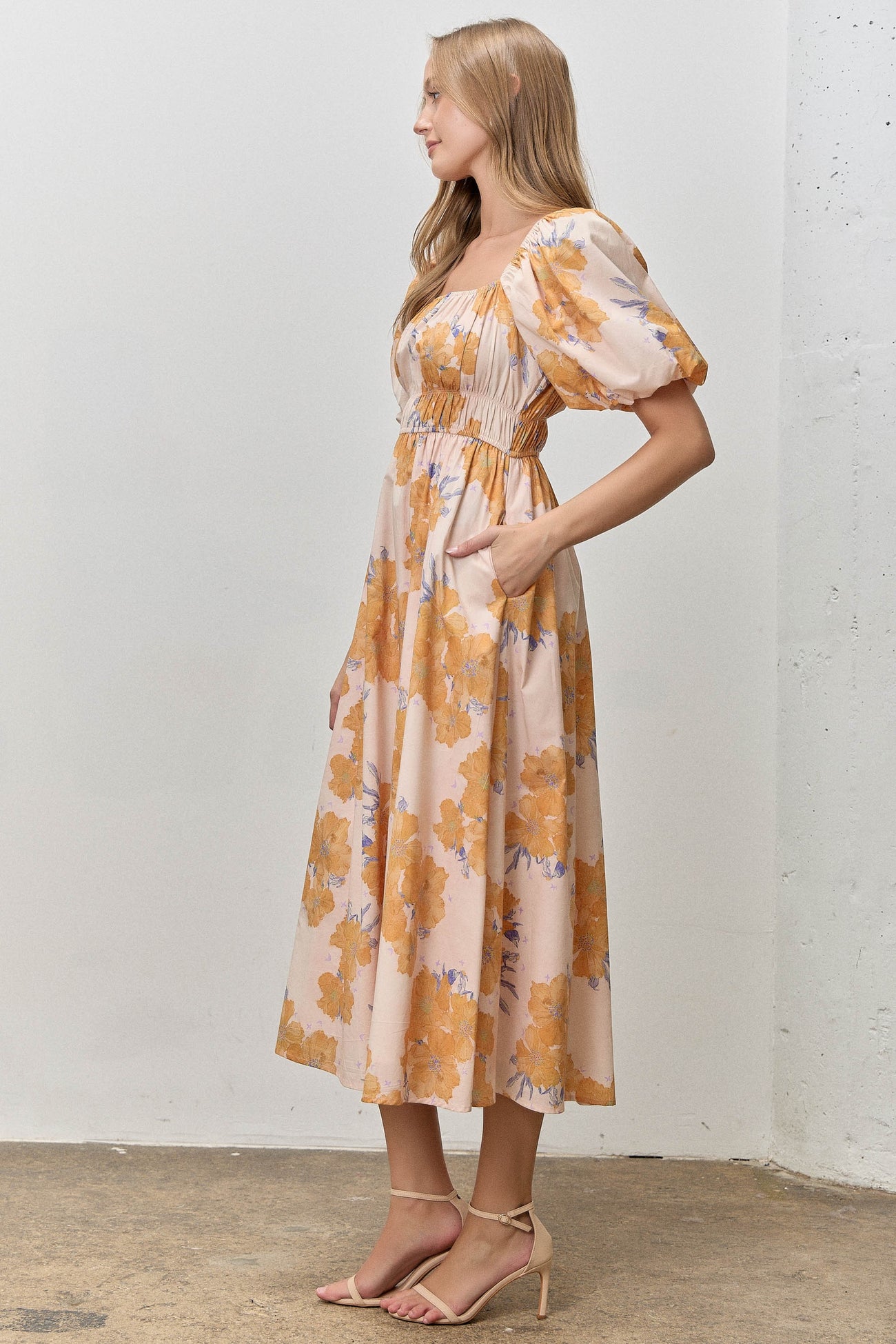 woman wearing a floral midi dress with puff sleeves and pockets in peach and orange tones
