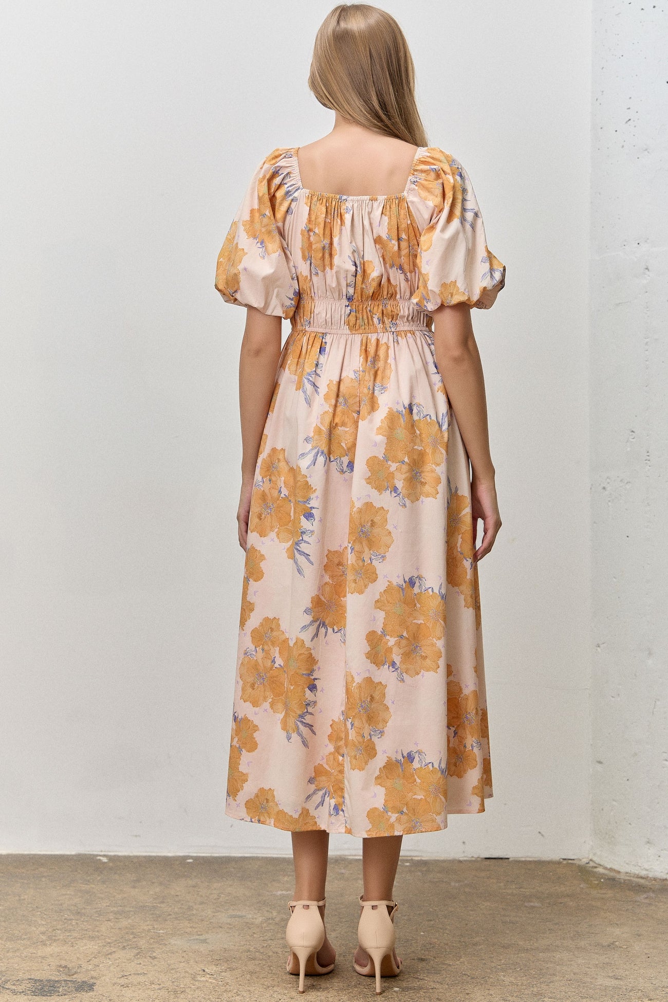 woman wearing a back view of a floral off-shoulder midi dress with puff sleeves in peach and orange tones