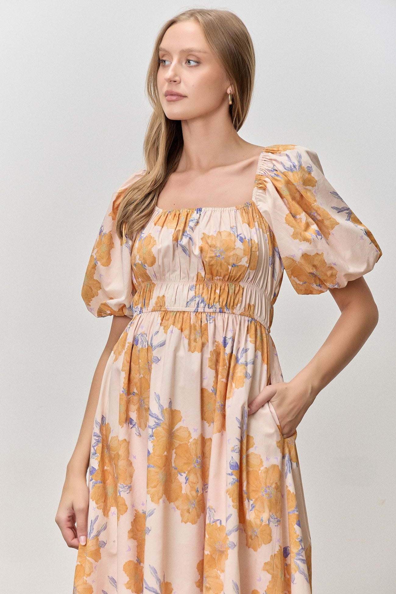 woman wearing a floral print midi dress with puff sleeves and a fitted bodice in peach and orange hues